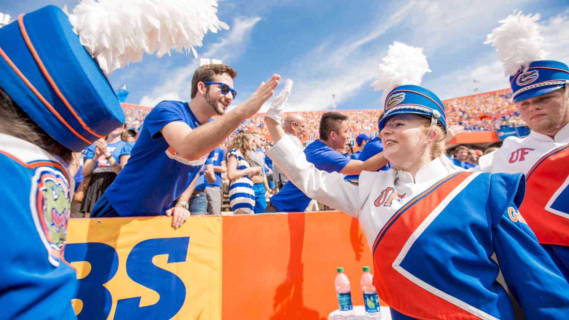 UF is home to the Pride of the Sunshine Gator Marching Band, one of the oldest and most prominent music ensembles on campus. [Alt text: Gator Band member in uniform high fives a student in the crowd at a football game as they run off the field following a pre-game performance.]